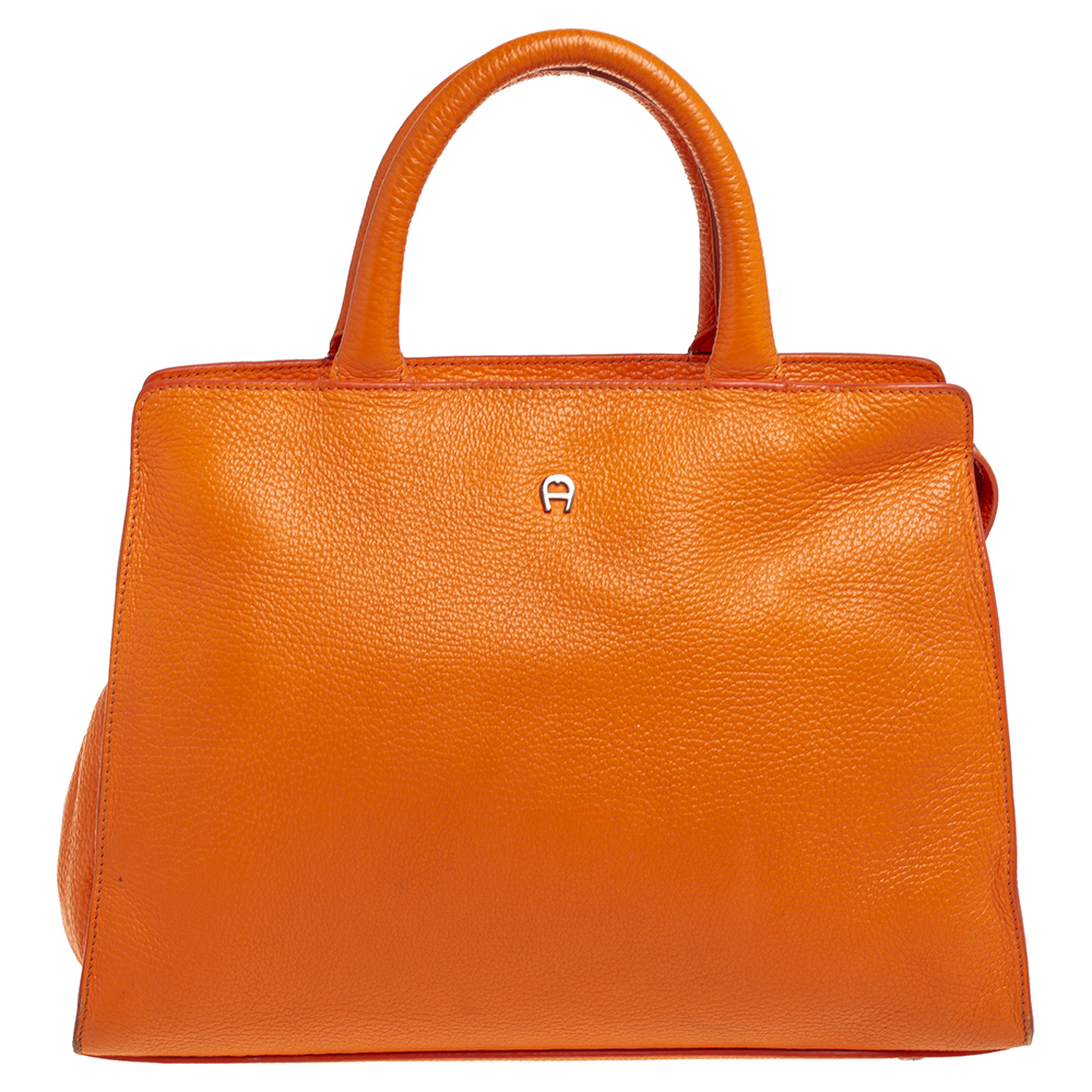 Characterized by its structured trapezoidal shape this Cybill tote by Aigner personifies elegance charm and sophistication. It is made from leather flaunting an orange shade and is designed minimally with a petite logo at the front in silver tone and two top handles. This tote is equipped with a fabric lined interior where you can house all your day to night essentials. Protective metal feet at the rear complete this creation.