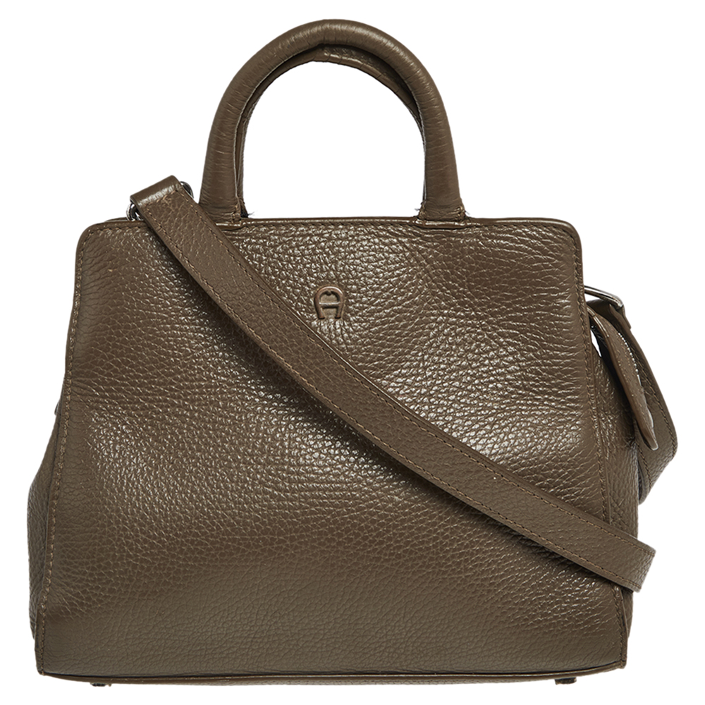 Characterized by its structured trapezoidal shape this Cybill tote by Aigner personifies elegance charm and sophistication. It is made from grained eather flaunting a timeless dark beige shade and is designed minimally with a petite logo at the front in silver tone and two top handles. This tote is equipped with a fabric lined interior where you can house all your day to night essentials. Protective metal feet at the rear complete this creation.