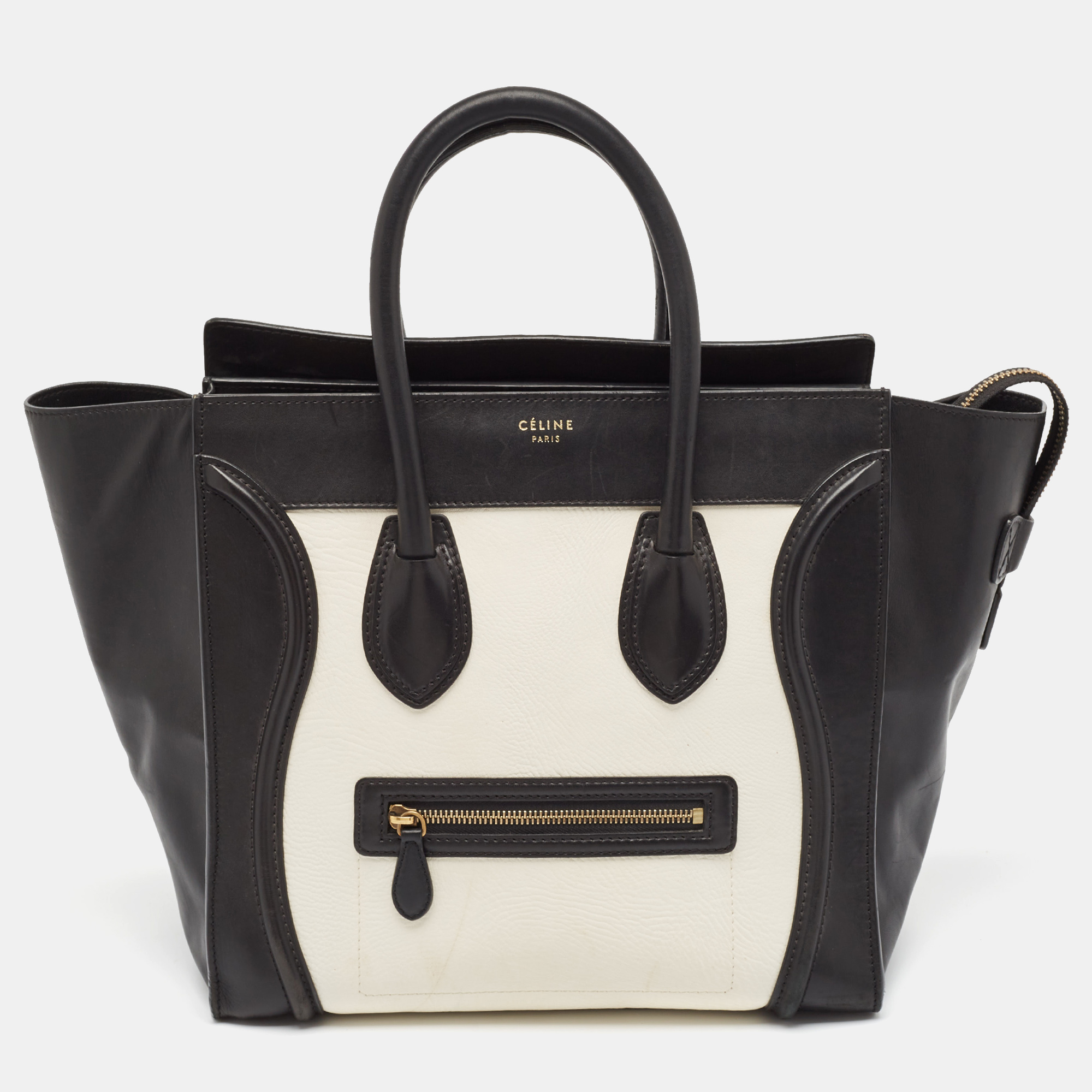 The usage of black and white leather on the exterior gives this Celine tote a high appeal. An eye catching accessory the bag features a front zipper pocket dual handles at the top and gold tone hardware. The leather lined interior is equipped to store more than just your phone and tiny essentials. The flappy wings at the sides and the brand signature on the front complete this design.