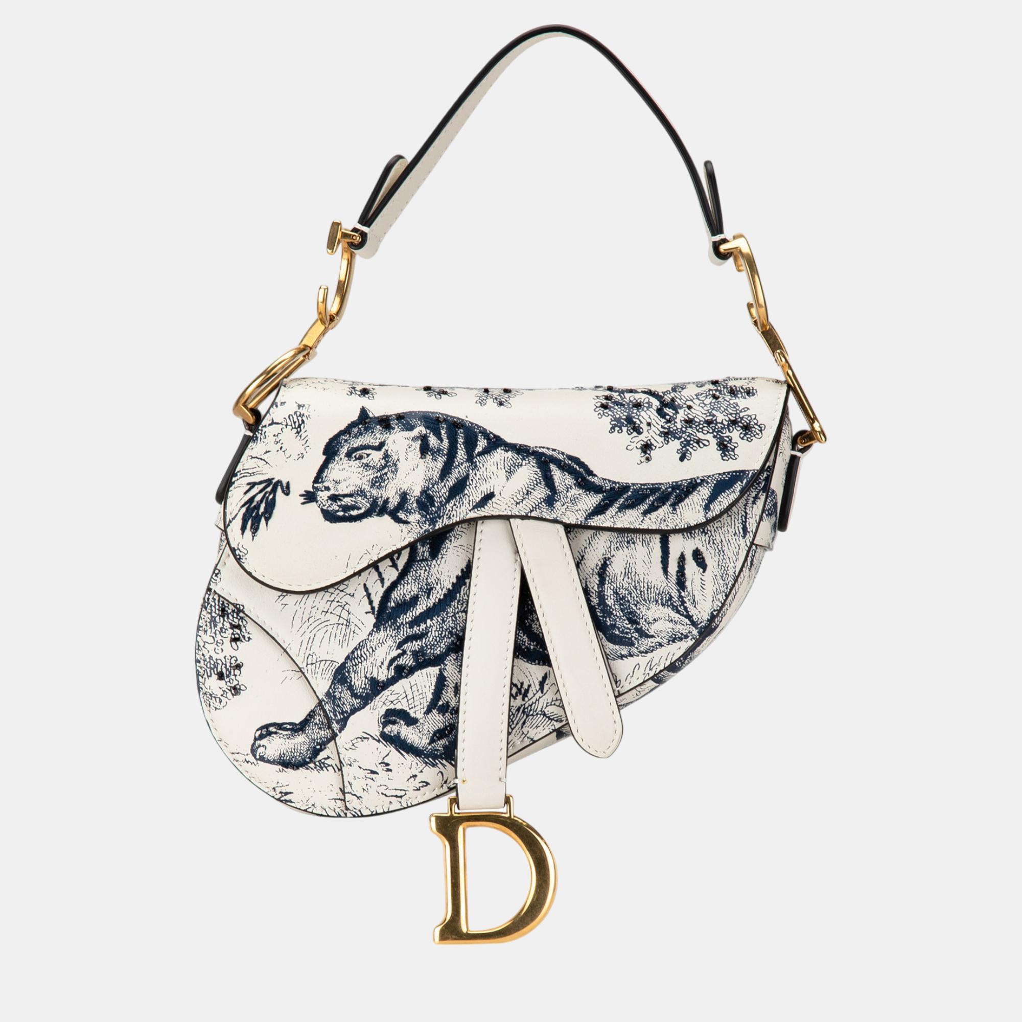 The Mini Toile de Jouy Saddle bag features a printed leather body a flat leather shoulder strap and a front flap with a magnetic snap closure.