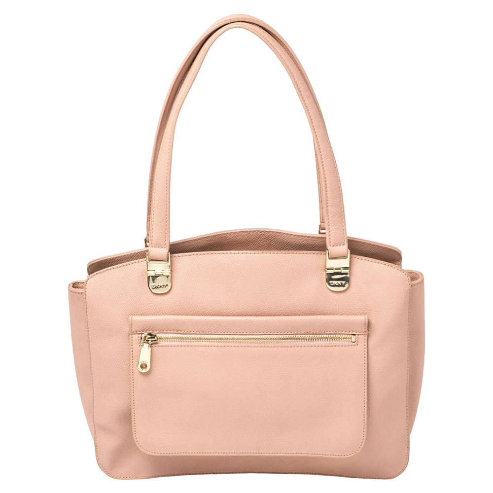 This DKNY tote has been designed for everyday use. Crafted from grained leather the pink tote features dual top handles a front zip pocket and protective metal feet at the bottom. The nylon lined interior houses three compartments for your necessities.