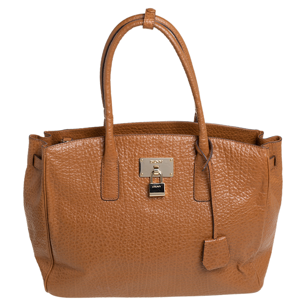 Timelessly elegant and stylish DKNYs collections capture the effortless nonchalant finesse of the modern woman. Crafted from leather in a caramel brown hue this chic tote features a compartmentalized interior with a padlock on the exterior. The sleek understated silhouette is punctuated with gold tone hardware.