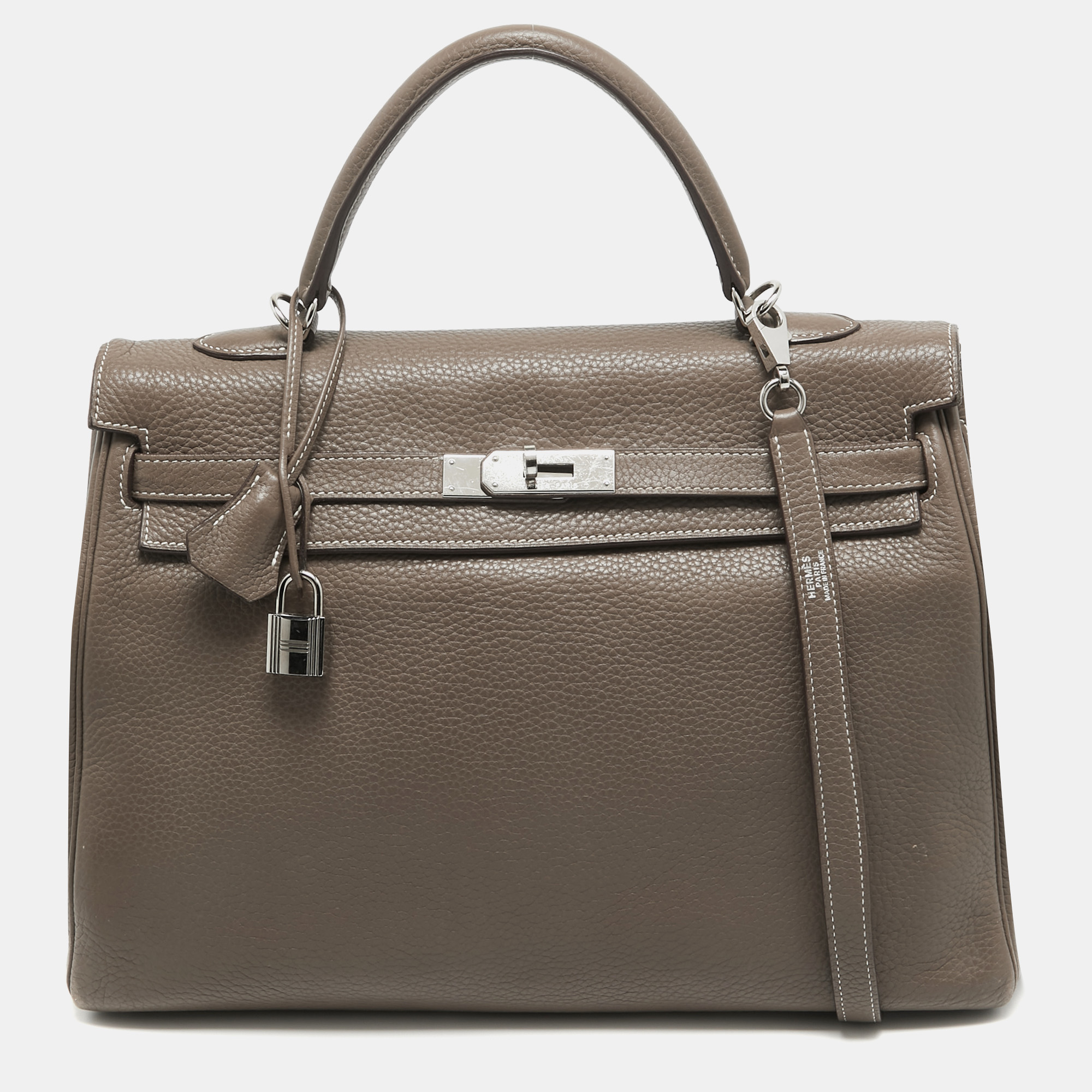 The Hermes Kelly is beautiful as it is carefully hand stitched to perfection. This Kelly Retourne is crafted from Taurillion Clemence leather and has palladium finish hardware. Retourne has a more casual look and is stitched on the inside thus making its edges softer. The bag comes with a turn lock closure single top rolled leather handle shoulder strap and a padlock with its keys within a clochette. The leather lined interior houses pockets and enough space to easily fit in all your daily necessities. Invest in this beauty today