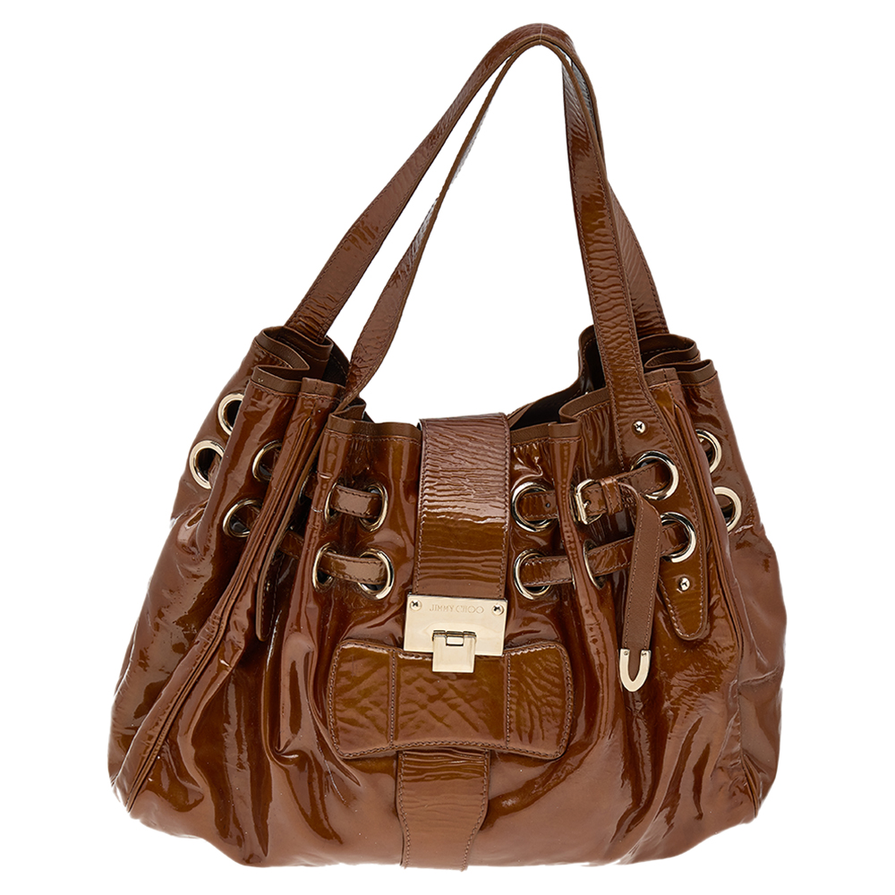 Own this gorgeous Jimmy Choo Riki bag today and light up your closet Crafted from patent leather this stunning brown number has a flap top with a signature lock and a spacious Alcantara interior. It also features two top handles gold tone hardware and dual belt detailing. Carry this beauty wherever you go and get set to receive admiring glances.