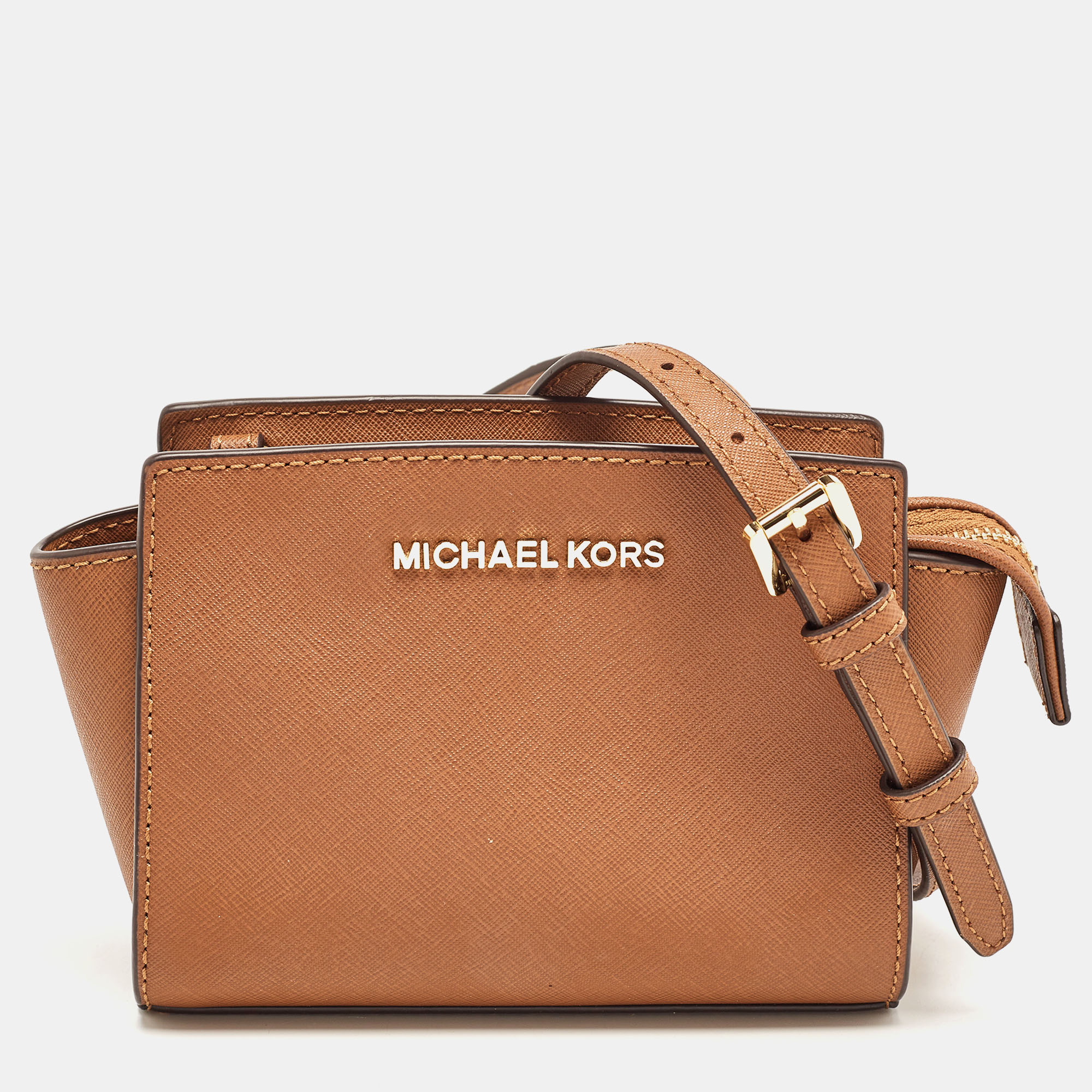 This mini Selma crossbody bag from Michael Kors is a stunning creation. It is designed using brown leather on the exterior and features a gold toned logo accent on the front and a shoulder strap. It is equipped with a fabric lined interior.