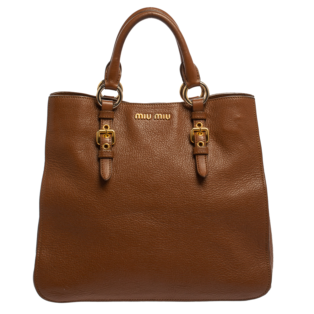 Stunning to look at and durable enough to accompany you wherever you go this Miu Miu tote bag is a joy to own This Madras bag is crafted from leather in a brown shade and is highlighted by gold tone hardware. Held by dual handles the creation is equipped with a fabric lined and perfectly sized to carry your belongings.