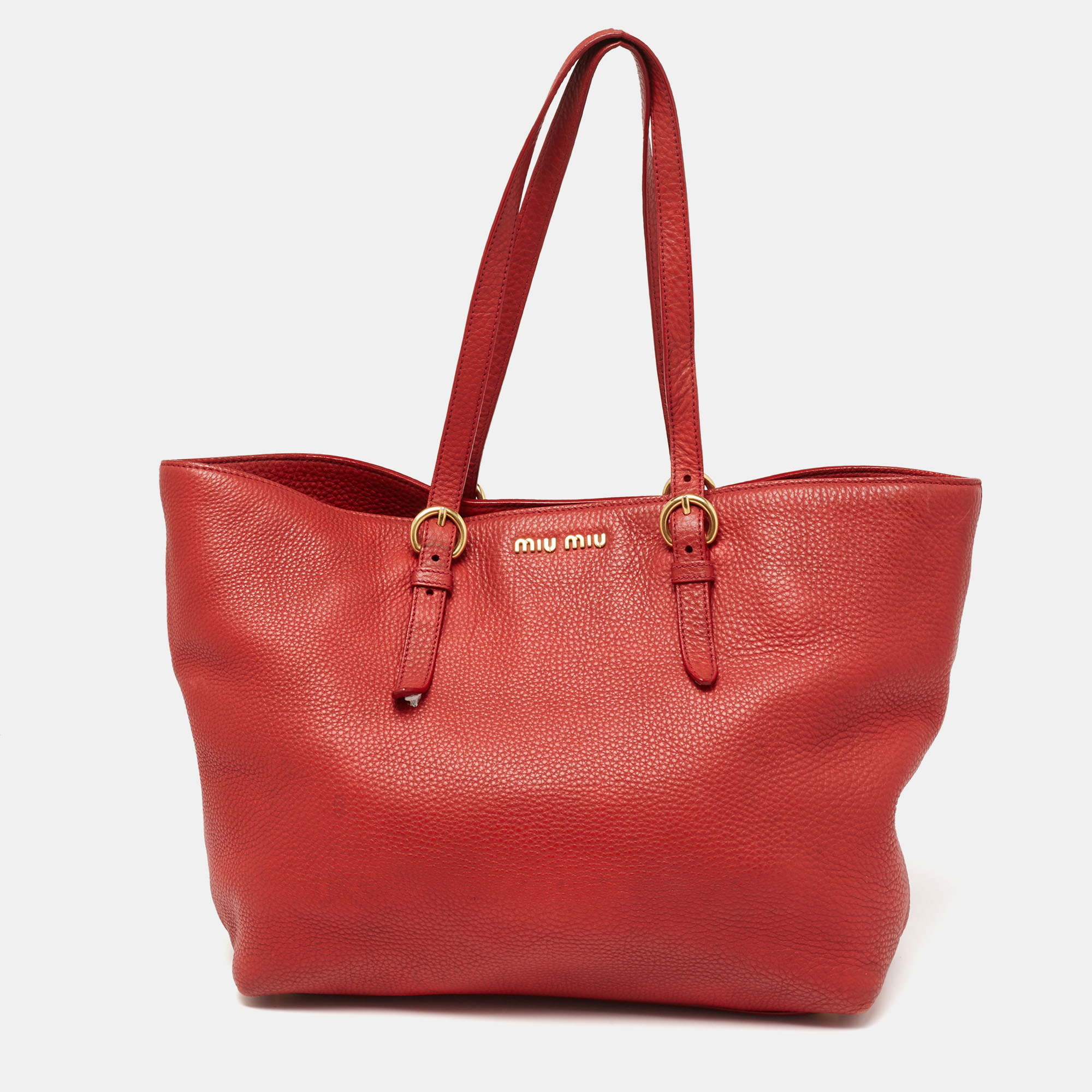 You don't have to worry about things missing or falling with this shopper tote from Miu Miu. Made from red leather this tote features two attached handles and a removable shoulder strap. The satin lined interior is sized to carry your belongings easily whether you are heading to work the mall or traveling.