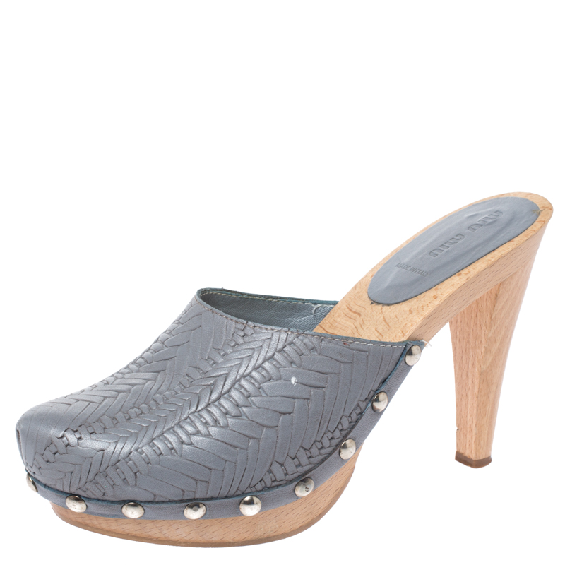 Made in Italy these platform clogs by Miu Miu are made from grey leather. The uppers are styled with a woven style and punctuated with large studs attached to the midsole. They have wooden platforms and 12.5 cm high block heels. It is finished with silver tone hardware leather lining and rubber soles.