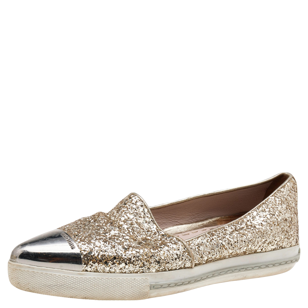 Exude class and luxury as you walk in these sneakers from the House of Miu Miu. These slip on style sneakers are created using gold glitter and metal on the exterior. They flaunt cap toes and silver tone hardware. These Miu Miu sneakers are truly trendy