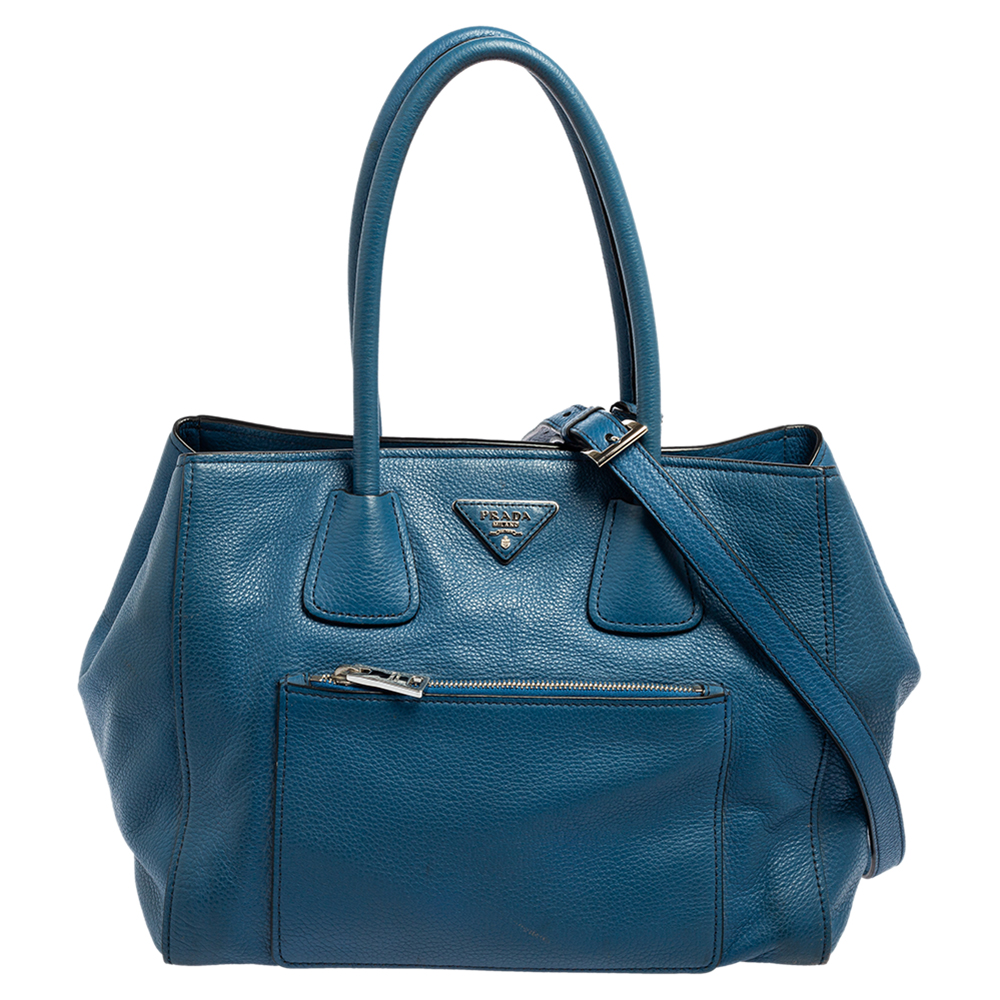 This Front Pocket Wing tote by Prada is an investment worthy creation. It is constructed using Vitello Daino leather in blue and equipped with two handles a front zip pocket and silver tone hardware. It has a nylon lined interior with a zip pocket and enough space for essentials.