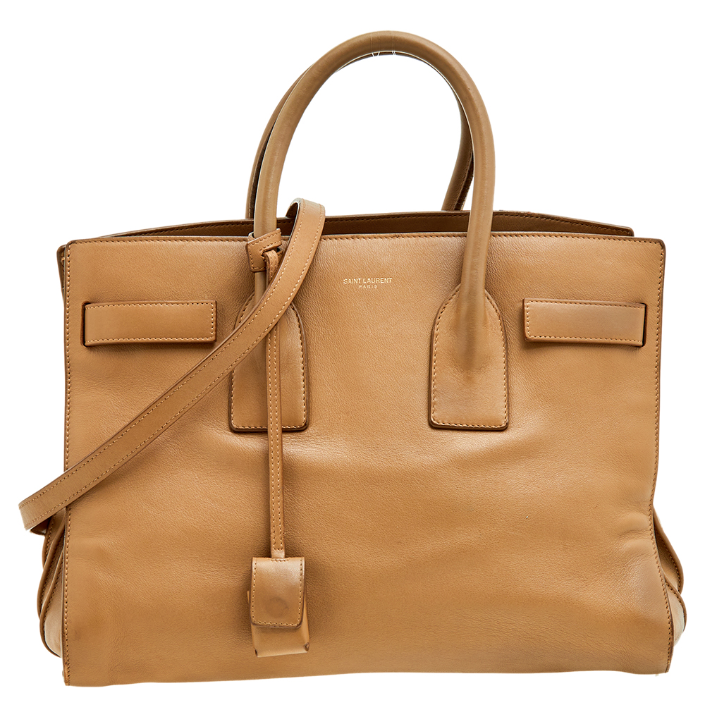 This Sac de Jour tote by Saint Laurent has a structure that simply spells sophistication. Crafted from beige leather the bag is held by double top handles. The tote comes with a suede lined interior with enough space to store your necessities and lastly the bottom comes secured with protective metal feet.