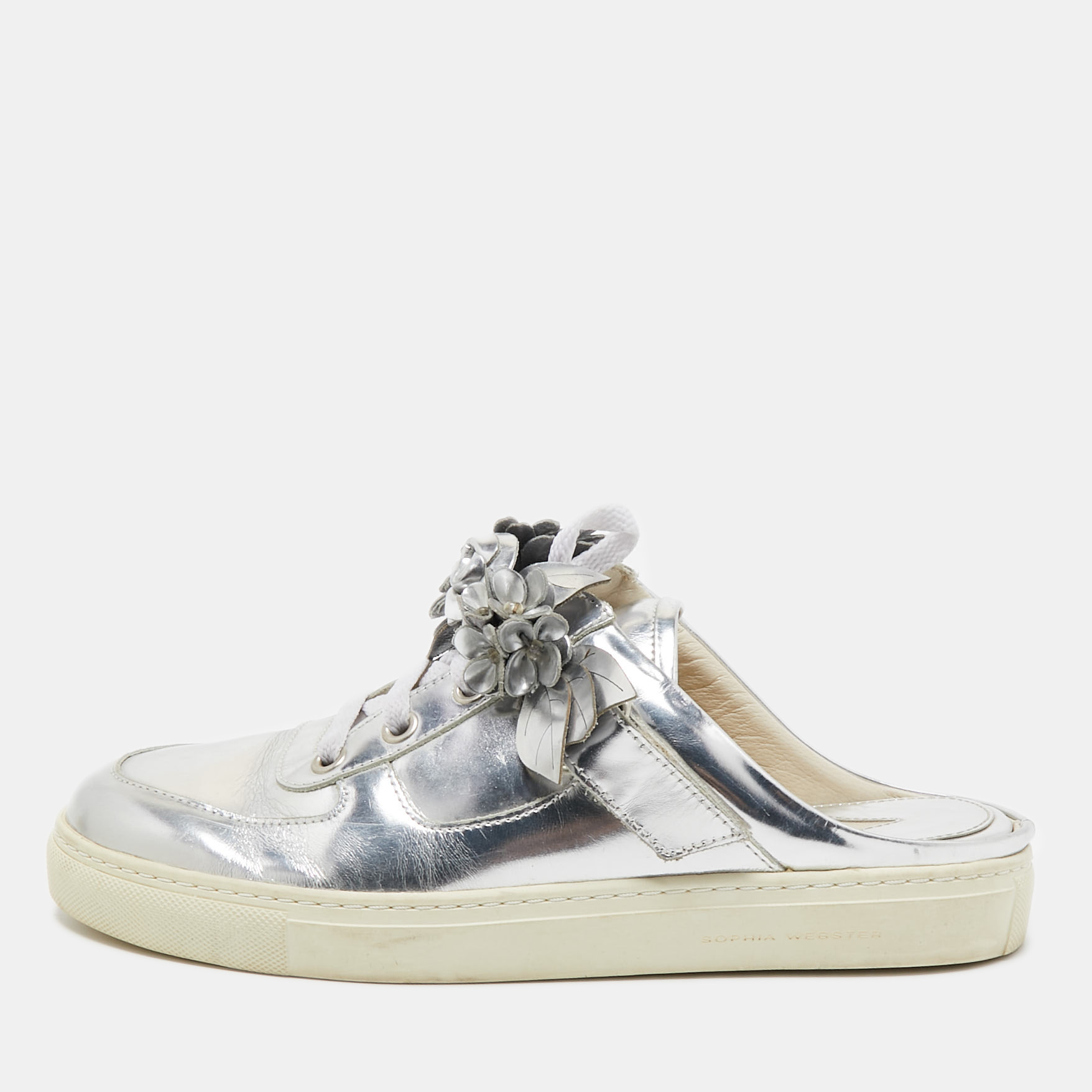 These mules from Sophia Webster are just right on trend They are crafted from metallic silver leather and designed in a slip on sneaker style with laces and flower appliques on the uppers. This eye catching pair is sure to have everyone in admiration.